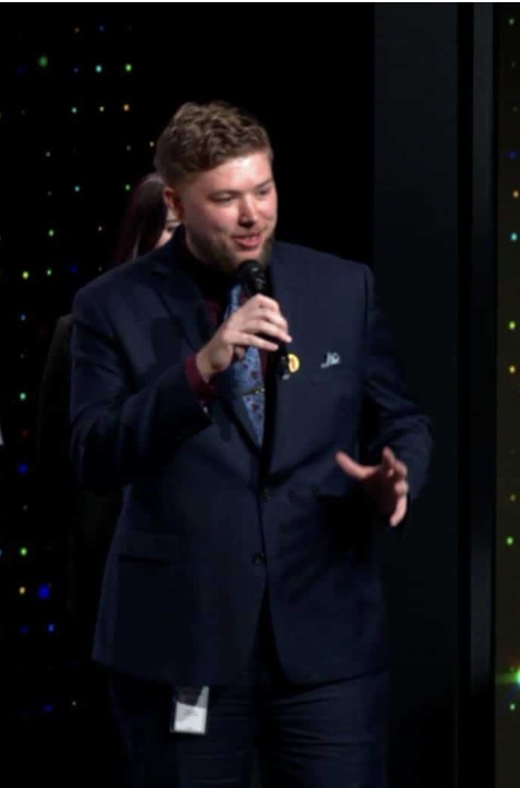 Marcus Gates in a navy suit speaking into a microphone on stage