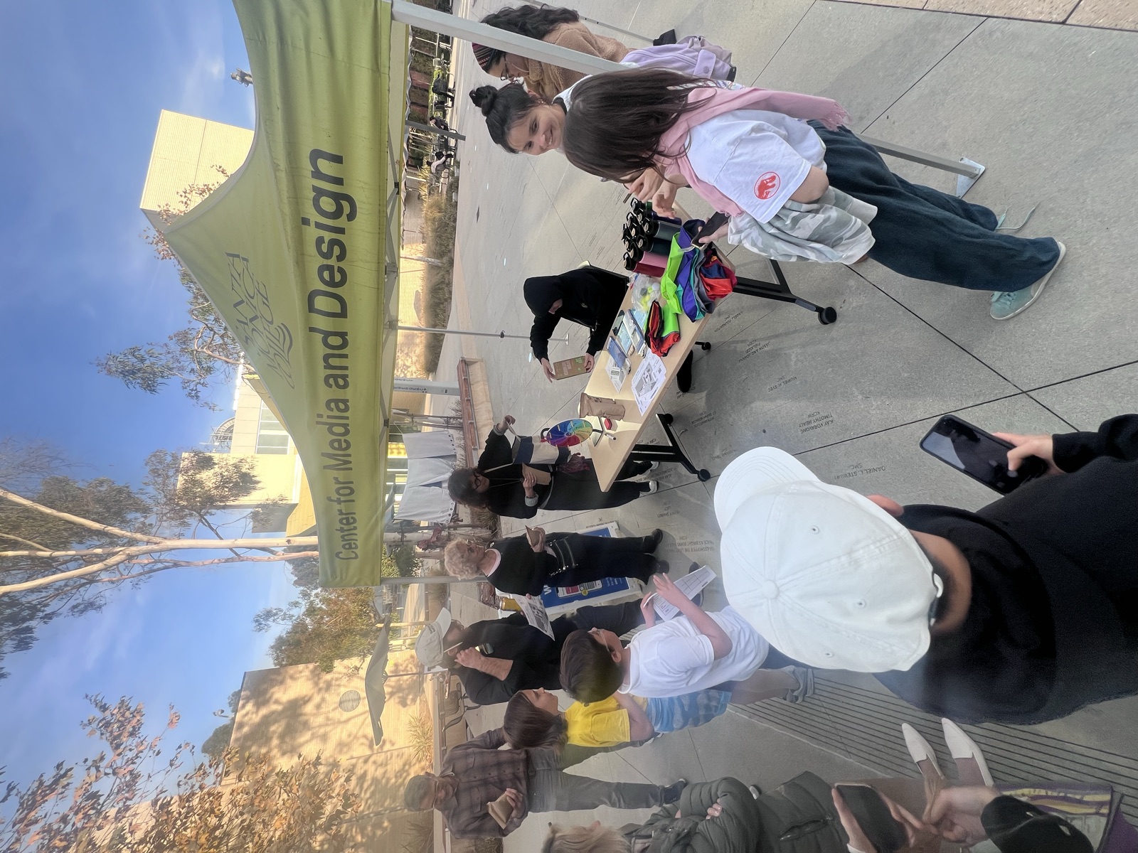 Visitors gathered around a table under a Center for Media and Design tent
